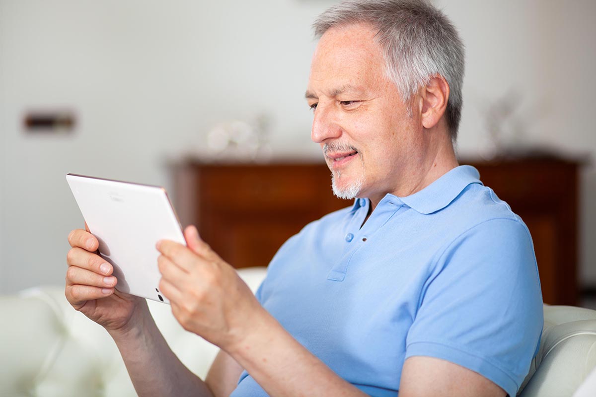 Portrait of a smiling mature man using his digital tablet while sitting on the couch